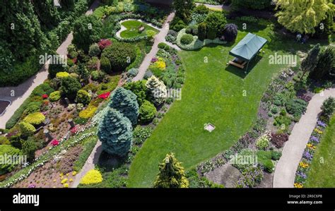 Vue aérienne d'un grand jardin avec différentes zones : pelouse, parterres de fleurs, et une tondeuse autotractée en action