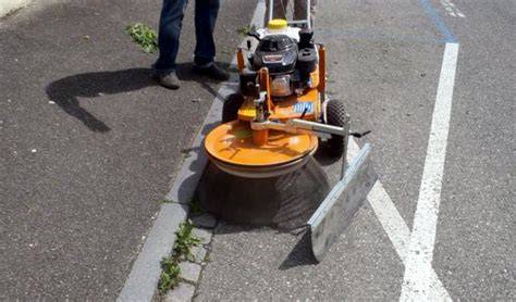 une brosse métallique désherbeuse en action sur des pavés