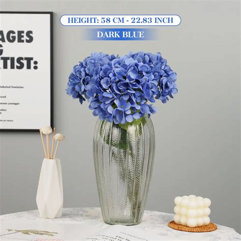 Un bouquet luxuriant d'hortensias artificiels en soie disposé dans un vase en verre sur une table de salon lumineuse