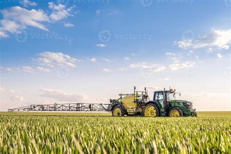 Champ de blé avec tracteur pulvérisateur en arrière-plan, habitations en premier plan