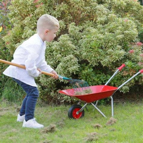 Enfant souriant poussant une brouette rouge dans un jardin