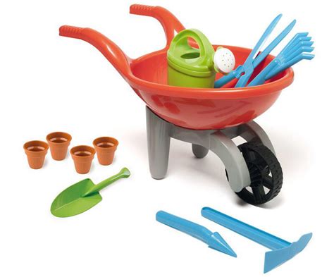 Un enfant jouant dans un jardin avec une petite brouette rouge en métal et des outils de jardinage adaptés.
