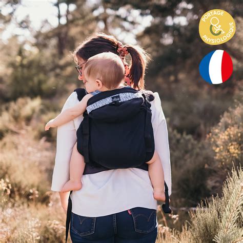 une maman portant son enfant dans un porte-bébé préformé physiologique lors d'une randonnée