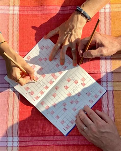 une personne concentrée remplissant une grille de mots fléchés avec un crayon