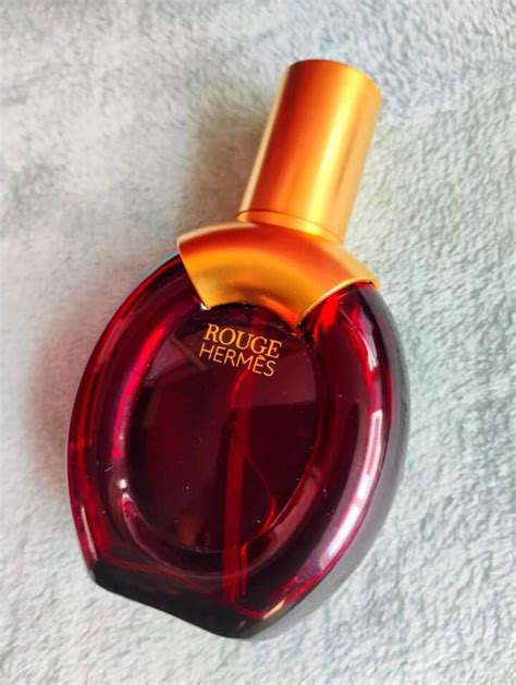 Flacon du parfum Rouge Hermès entouré d'ingrédients olfactifs comme la rose, la vanille et l'ylang-ylang
