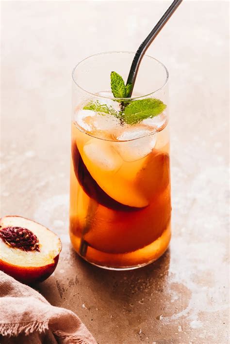 Un verre de thé glacé à la gaulthérie, décoré avec des fleurs séchées de rose et une tranche de citron, posé sur une surface naturelle.