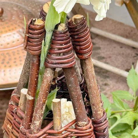 Un tipi en bois de noisetier supportant des fleurs grimpantes dans un jardin fleuri