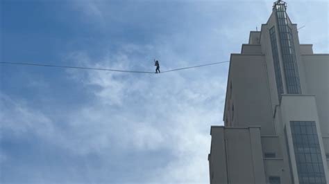 Un funambule évoluant sur un câble tendu entre deux édifices urbains