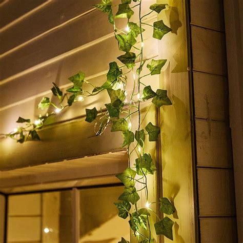 Une guirlande de lierre artificiel entrelacée de microLEDs installée sur une pergola de terrasse en soirée.
