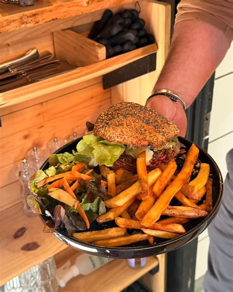 Une vue panoramique d'un burger artisanal généreusement garni avec des frites maison dorées, illustrant la signature culinaire du Mirabelle.