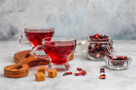 une tasse d'infusion églantier hibiscus fumante avec des baies d'églantier et des fleurs d'hibiscus séchées à côté