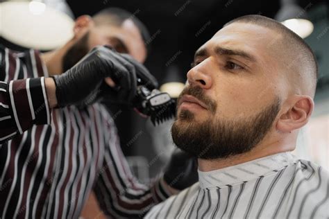 Un barbier travaillant avec une tondeuse sur la barbe d'un client