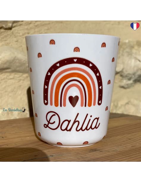 Image d'un gobelet personnalisé avec un logo d'école et un prénom, mis en évidence par rapport à des gobelets jetables empilés.