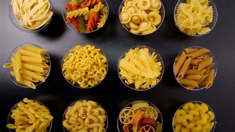 Diverses pâtes italiennes comme des fusilli, des penne et des spaghettis, mélangées avec des sauces colorées et des herbes aromatiques.