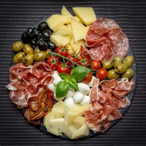 Une sélection d'antipasti italiens, comprenant des olives, des fromages, de la charcuterie et des légumes grillés, disposés sur un plateau en bois.