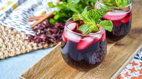 Verre de jus de bissap rouge vif avec des feuilles de menthe et des fleurs d'hibiscus séchées en arrière-plan