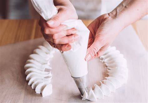 gros plan sur le pochage de la chantilly bicolore sur un palet breton, illustrant la précision du geste et la texture onctueuse de la crème