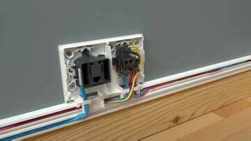 Photo montrant l'installation d'une goulotte en PVC sur un mur blanc