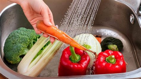 Illustration of various fruits and vegetables being washed under running water with a clean brush