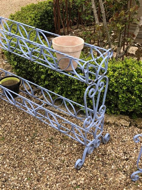Illustration montrant une jardinière en fer forgé fixée sur un balcon avec des plantes fleuries